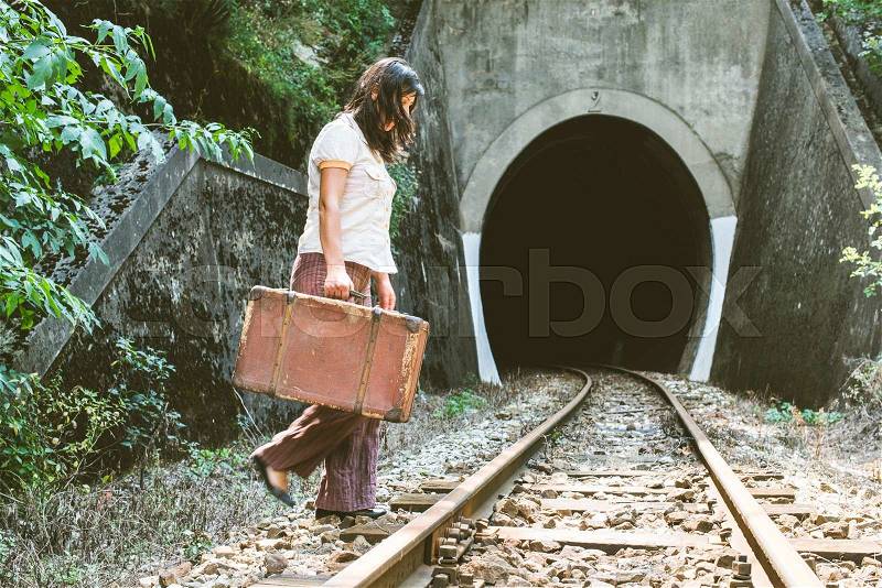 Woman walk on railroad with a suitcase in hands. Vintage style image, stock photo