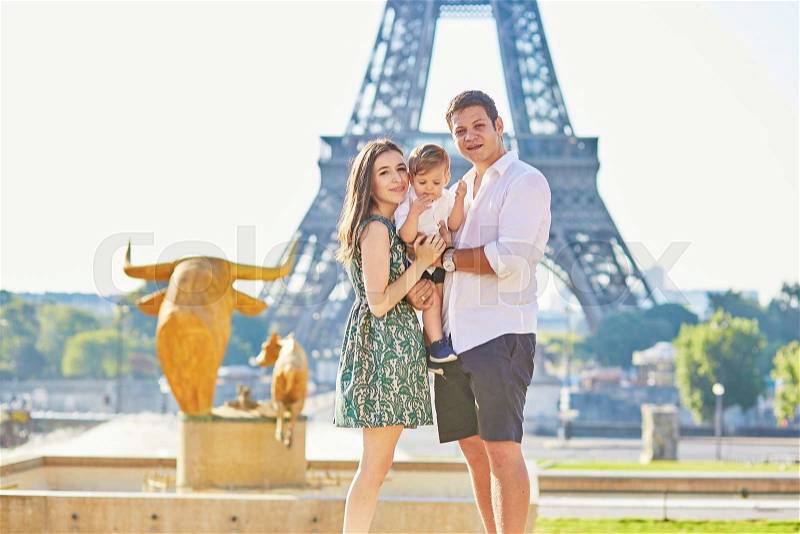 Happy family of three standing in front of the Eiffel tower and enjoying their vacation in Paris, France, stock photo