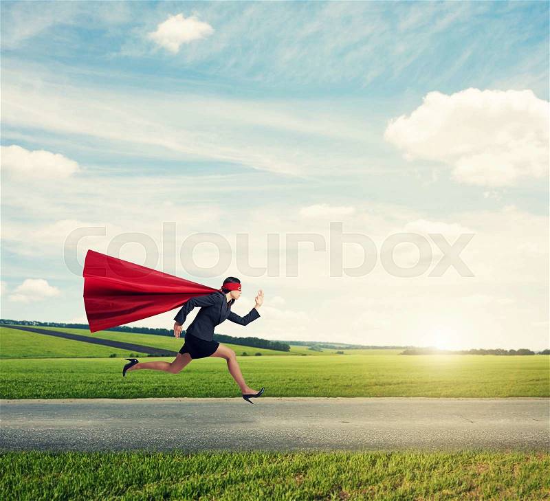 Concentrated superwoman in formal wear and red cloak with mask fast running on the road at outdoor, stock photo
