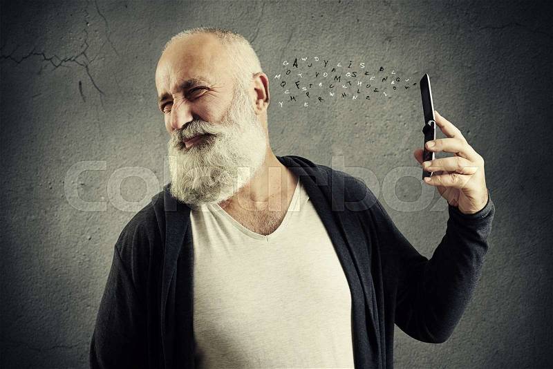 Small drawn letters flying to discontented senior man from his cellphone over dark wall , stock photo