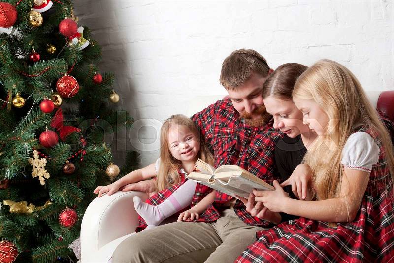 Parents and children reading stories together. Family sitting on the couch beside Christmas tree, stock photo