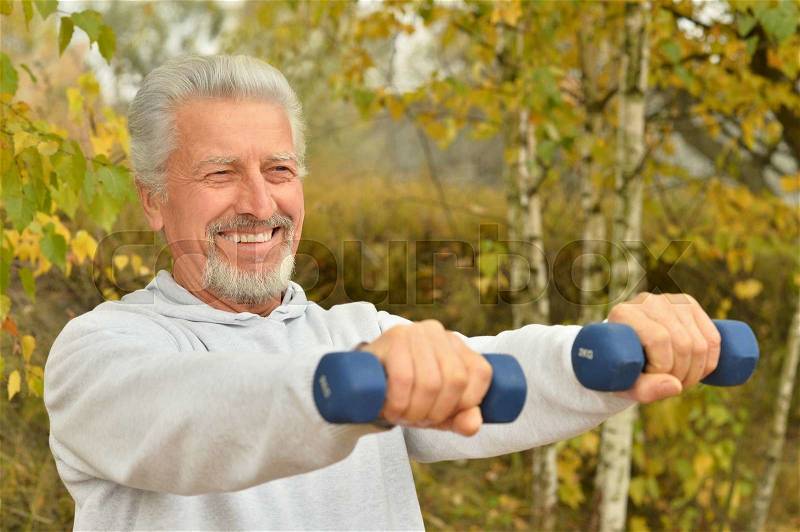 Elderly man exercising with dumbbells in autumn park, stock photo