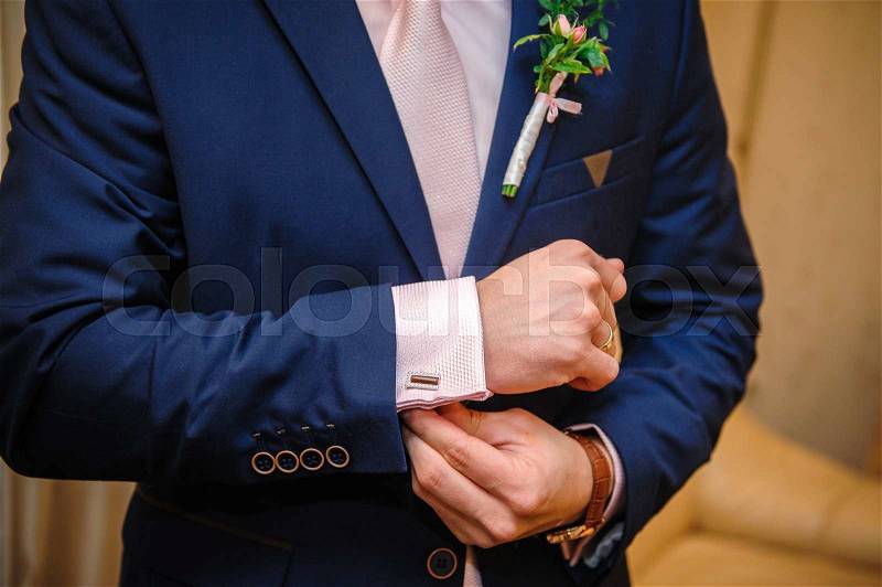 Groom in a suit hands wear cufflinks in room, stock photo
