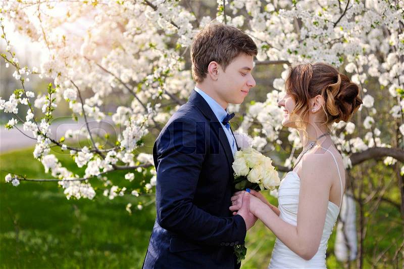 Bride and groom look at each other in the blossoming spring garden, stock photo