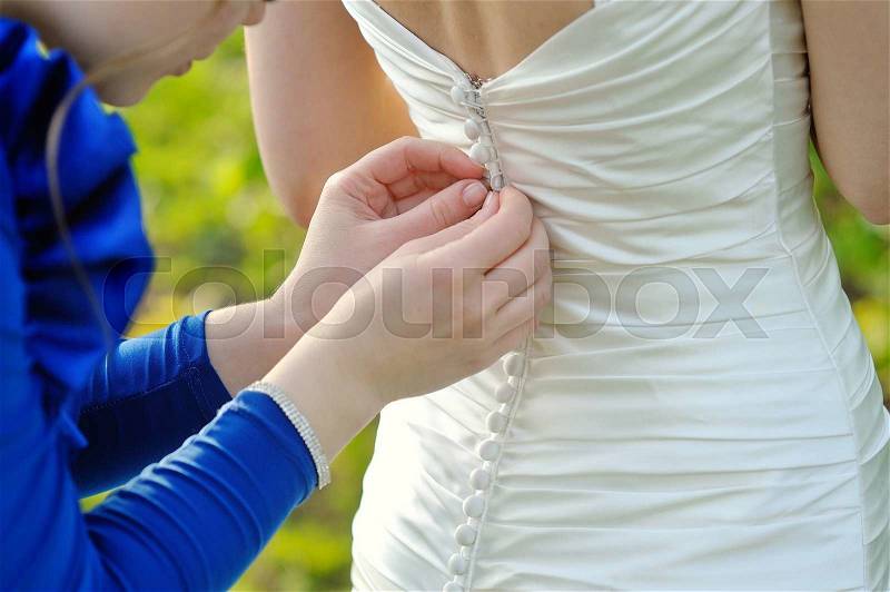 Bridesmaid helping to dress the bride on the wedding day, stock photo