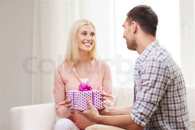 Relationships, love, people, birthday and holidays concept - happy man giving woman gift box at home, stock photo
