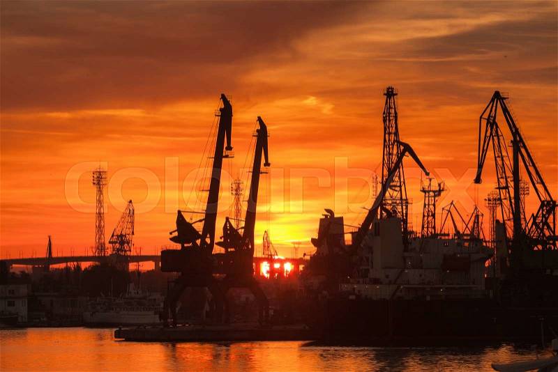 Silhouettes of cranes and cargo ships in port of Varna at sunset under bright red sky, stock photo