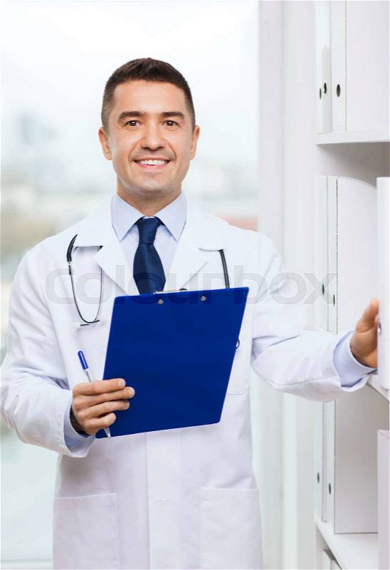 Medicine, profession, technology and people concept - happy male doctor with clipboard in medical office, stock photo