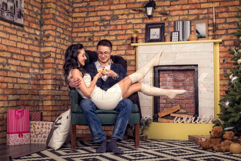 Young man make marriage proposal to girlfriend at Christmas.Guy gives the girl a small box gift Christmas Eve. Girl sits on the lap of man with raised legs.Pair stylish smiling and enjoys the holiday, stock photo