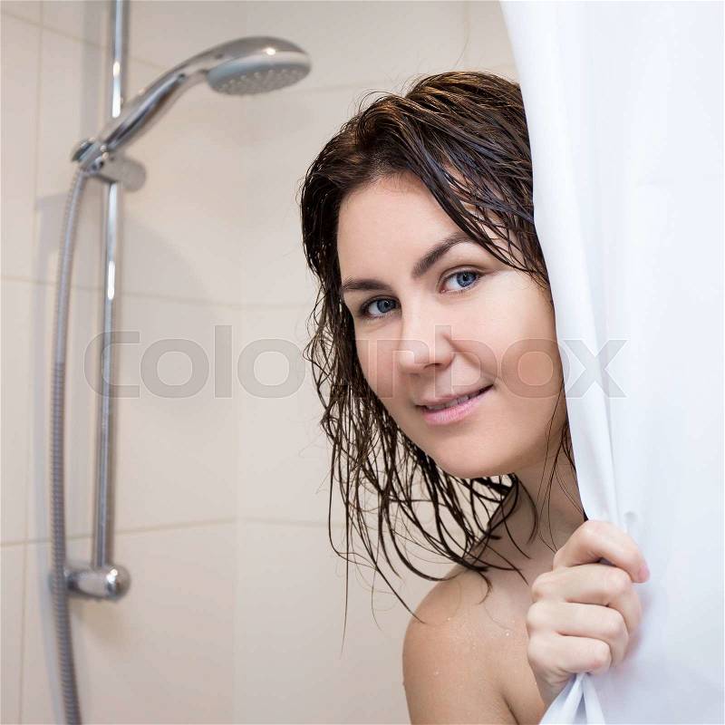Young beautiful woman standing in shower and covering herself with curtain, stock photo
