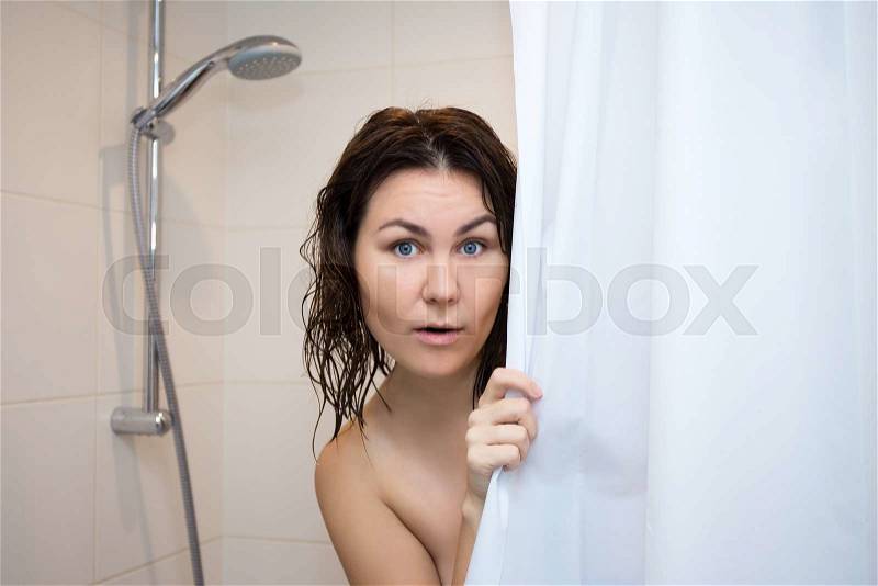 Young beautiful scared woman hiding behind shower curtain, stock photo