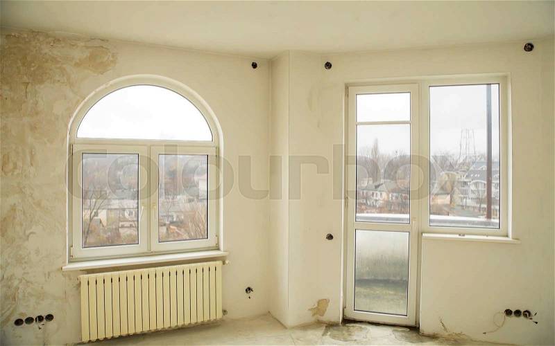 An empty interior of a nearly finished apartment with white walls and big windows, stock photo