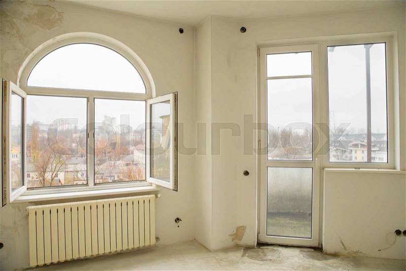 An empty interior of a nearly finished apartment with white walls and big windows, stock photo