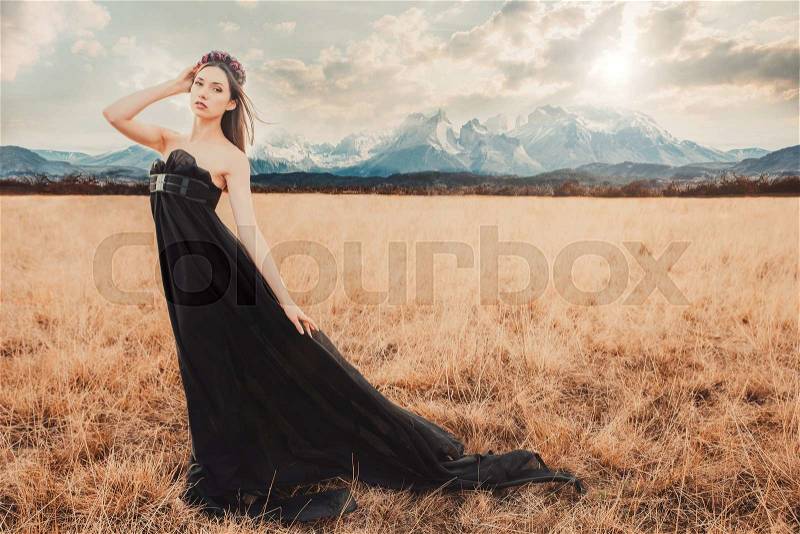 Beautiful girl in a black dress with flowers in the mountains in the background. Fashion shot, stock photo