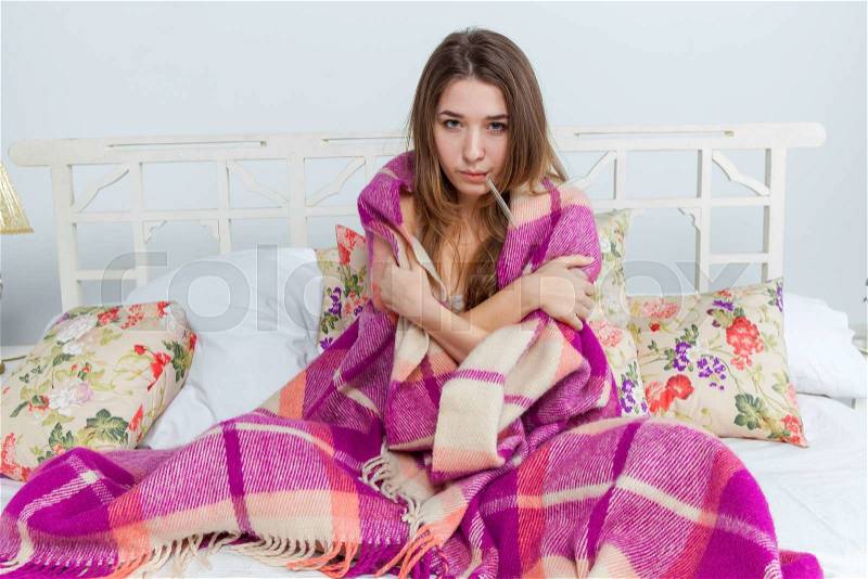 Young sick woman in blanket with thermometer in bed at home, stock photo