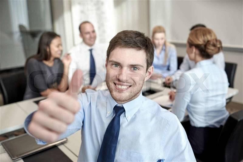 Business, people, gesture and teamwork concept - smiling businessman showing thumbs up with group of businesspeople meeting in office, stock photo