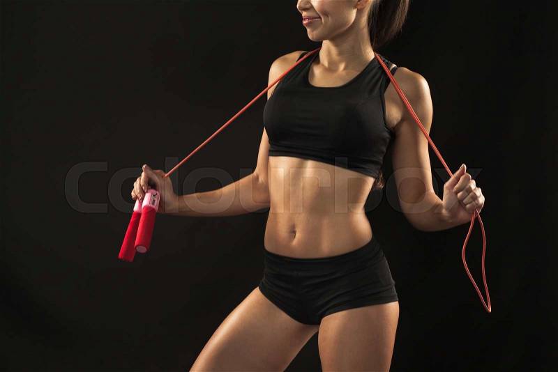 Muscular young woman athlete with a skipping rope on black background. belly closeup, stock photo