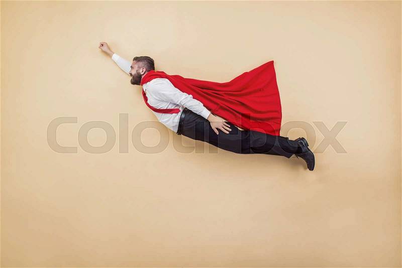 Manager in a superman pose wearing a red cloak. Studio shot on a beige background, stock photo