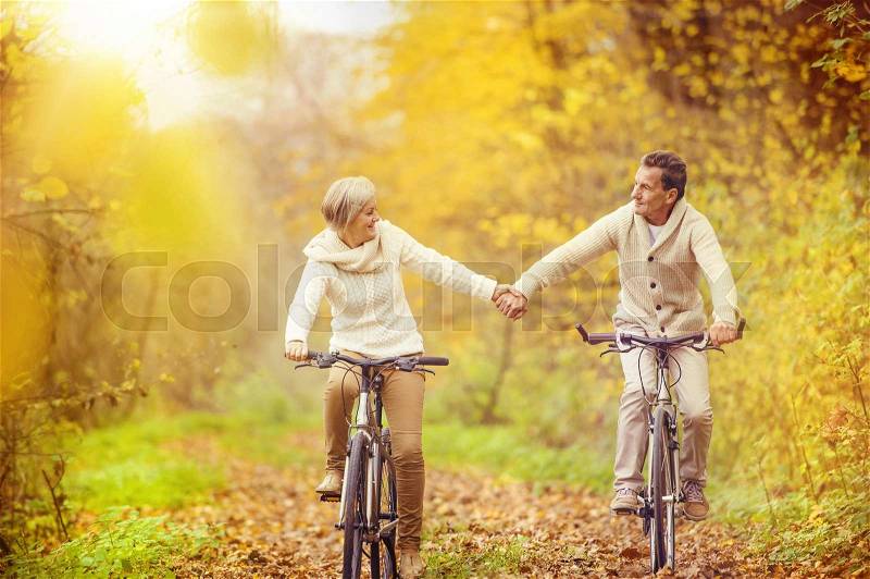 Active seniors riding bike in autumn nature. They relax outdoor, stock photo