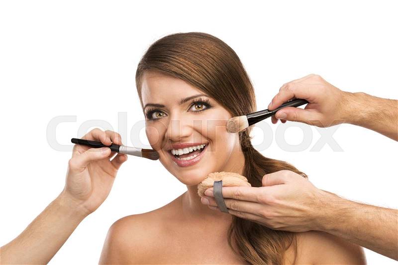 Portrait of beautiful woman with makeup brushes near attractive face, many hands applying make up on woman face isolated on white background, stock photo
