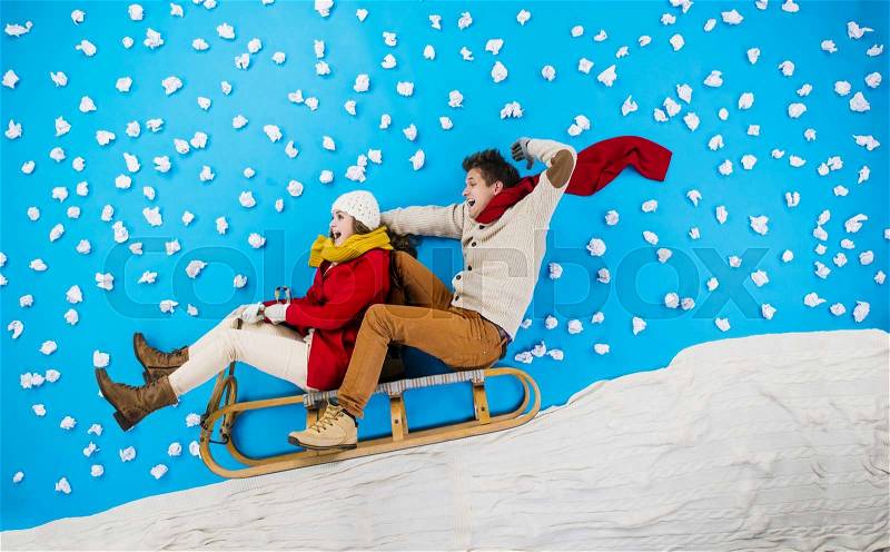Happy young couple on sledge having fun against the blue background with snowflakes, stock photo