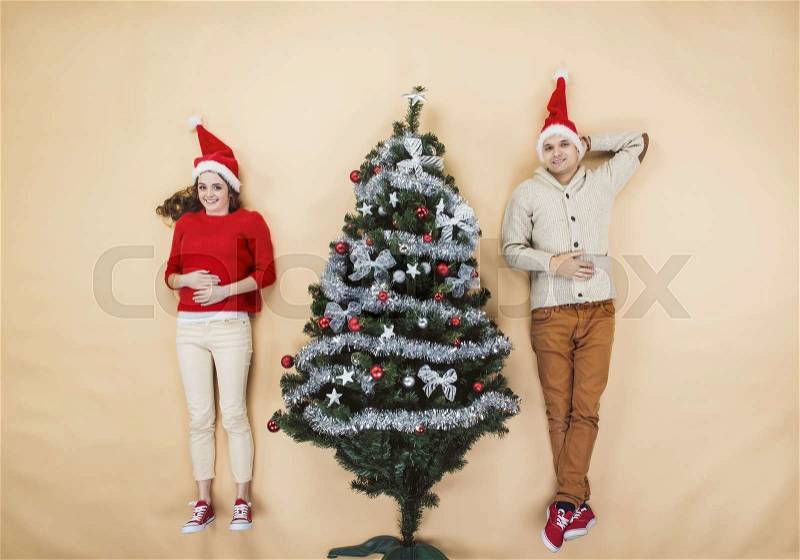 Happy young couple next to the Christmas tree against the beige background, stock photo