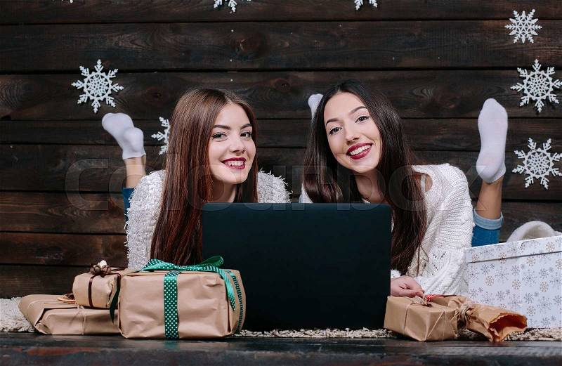Two beautiful girls lie on the floor with a laptop, between gifts for Christmas, stock photo