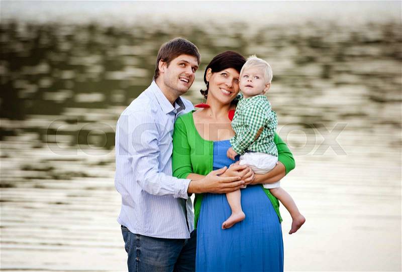 Happy young family spending summer time together by the lake on the sandy beach, stock photo