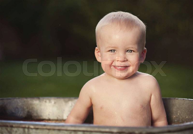 Cute funny little boy bathing in galvanized tub outdoor in green garden, stock photo