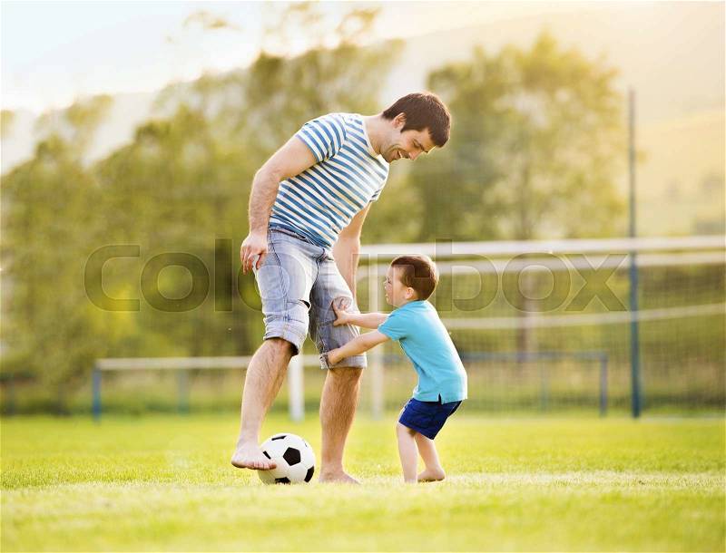 Young father with his little son playing football on football pitch, stock photo