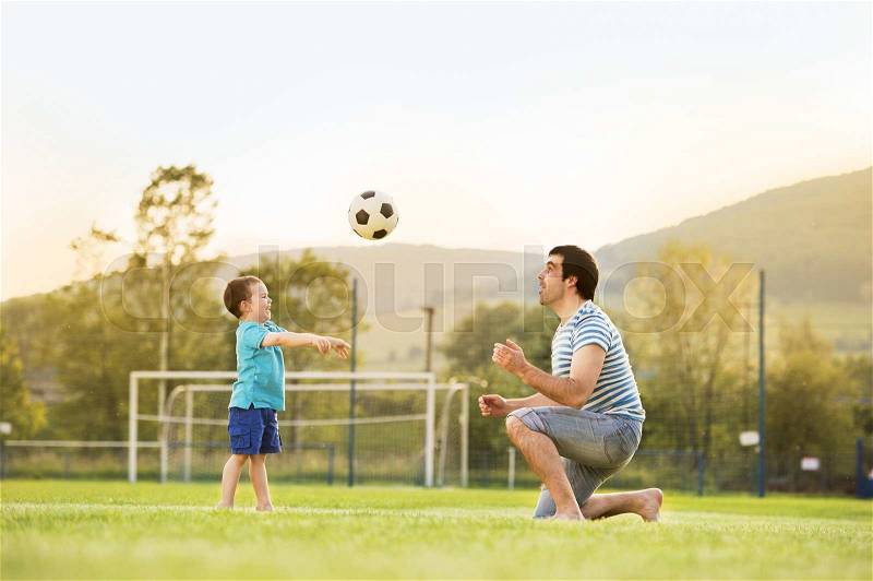 Young father with his little son playing football on football pitch, stock photo