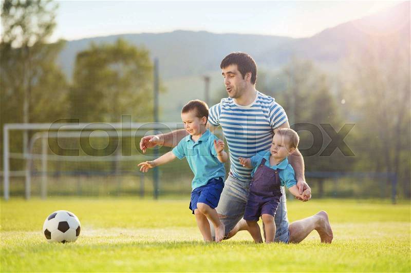 Young father with his little sons playing football on football pitch, stock photo