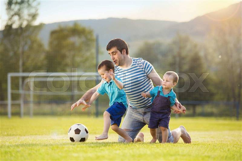 Young father with his little sons playing football on football pitch, stock photo