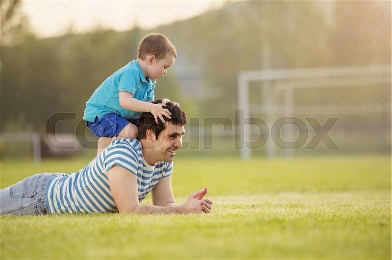 Young father with his little son having fun on football pitch, stock photo