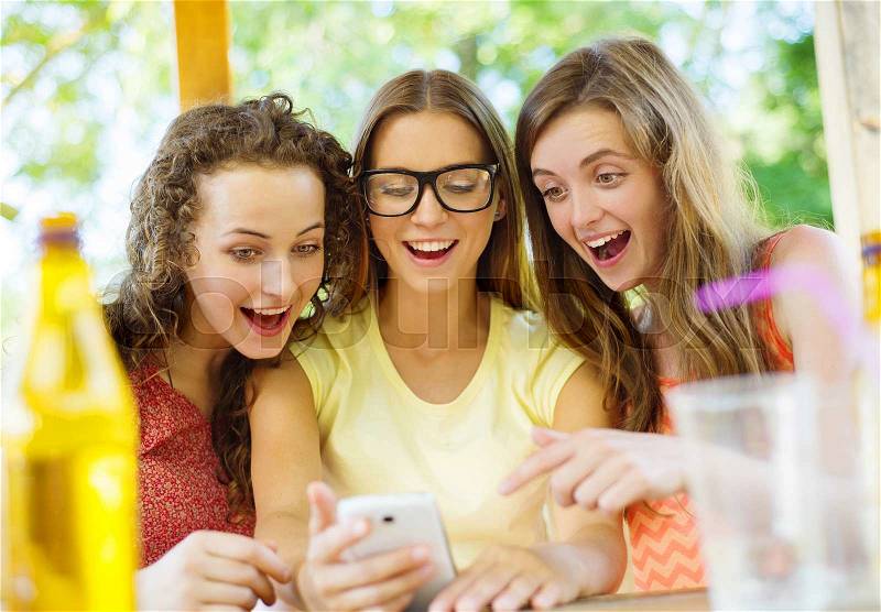 Three beautiful girls drinking and having fun with smartphone in pub garden, stock photo