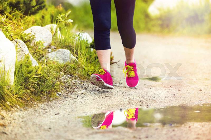 Senior runner woman feet running in beautiful nature reflecting in puddle, closeup on feet, stock photo