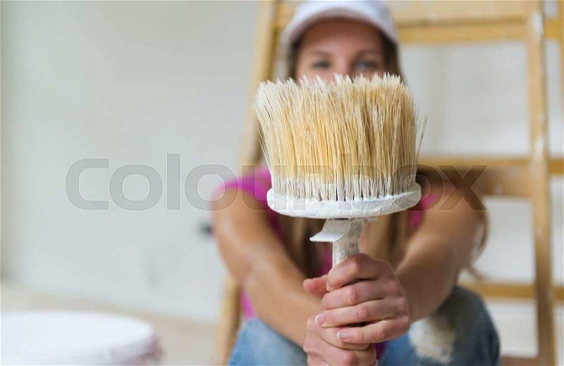 Happy smiling woman sitting on the floor and having a break from painting, stock photo