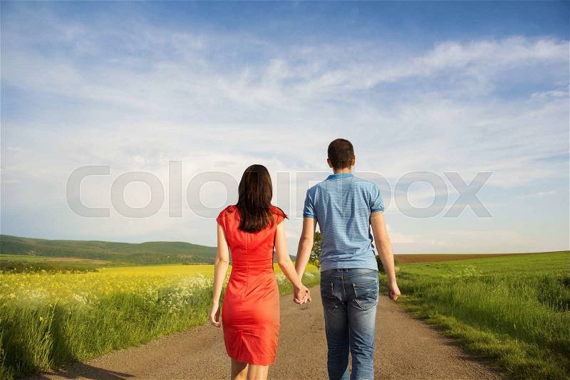 Happy young couple in love walking and holding hands on countryside road next to the colza field, stock photo