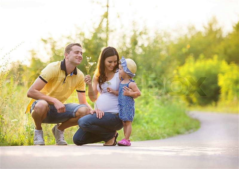 Happy pregnant family with little daughter spending time together in summer nature, stock photo