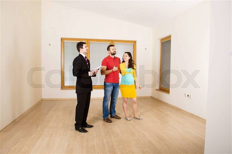 Young couple is sitting on the floor in their empty new house. Woman is pregnant, stock photo