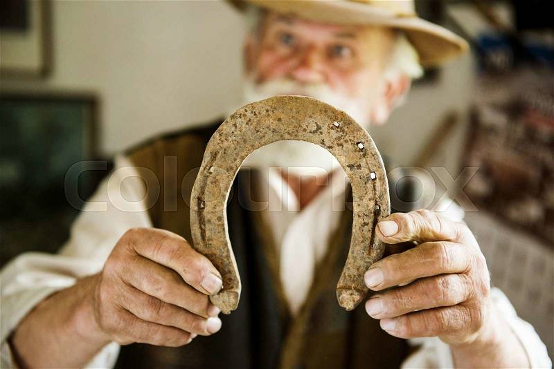 Old farmer with beard and hat holding horseshoe, stock photo