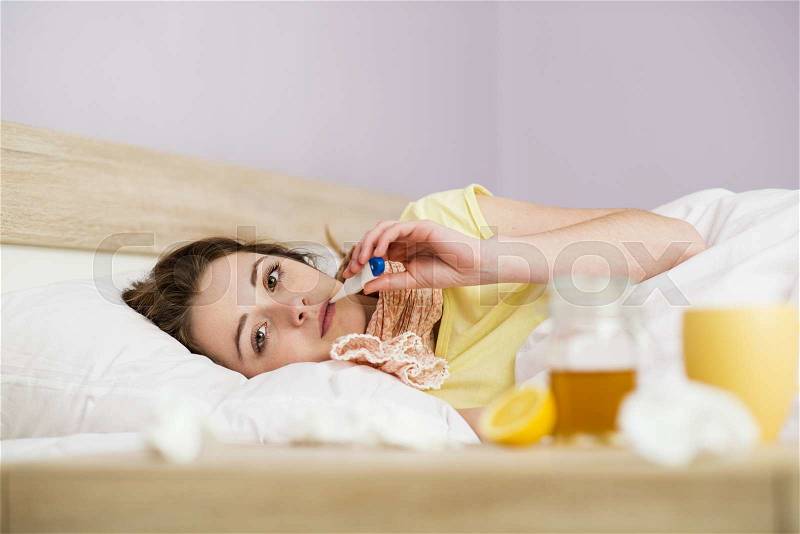 Sick woman lying in bed with high fever. She has cold and flu. In front of her is tea with lemon and honey, stock photo