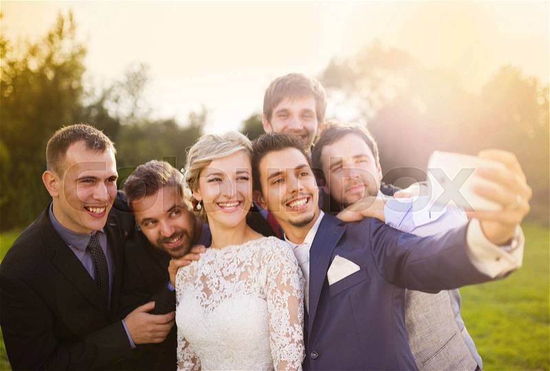 Outdoor portrait of beautiful young bride with groom and his friends taking selfie, stock photo