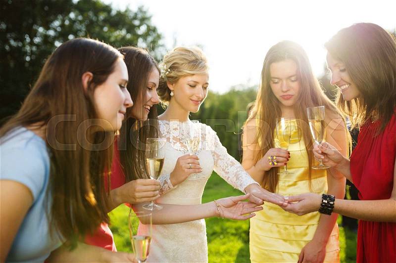 Happy bride is showing her wedding ring to her friends at the wedding reception outside, stock photo