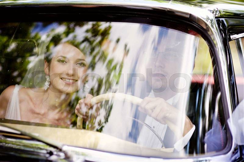 The bride and groom have fun behind the wheel of retro car, stock photo