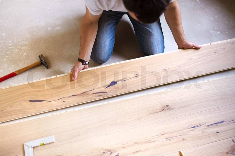 Unrecognizable handyman installing wooden floor in new house, stock photo
