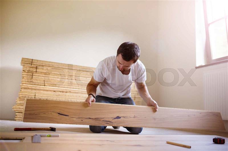 Young handyman installing wooden floor in new house, stock photo
