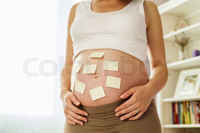 Close-up of unrecognizable pregnant woman with copy space sticky notes on her belly, stock photo