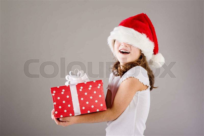 Happy small girl in santa hat with christmas gift, stock photo