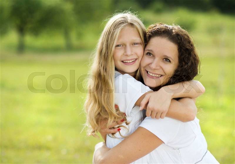 Mother and teenage daughter hugging and smiling together in summer garden, stock photo